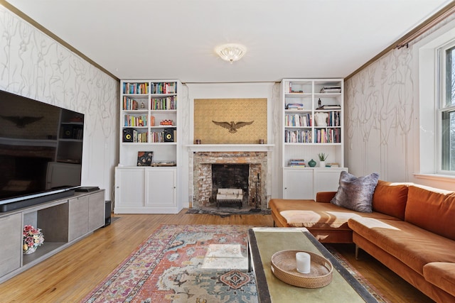 living area with a brick fireplace, wood finished floors, crown molding, and wallpapered walls