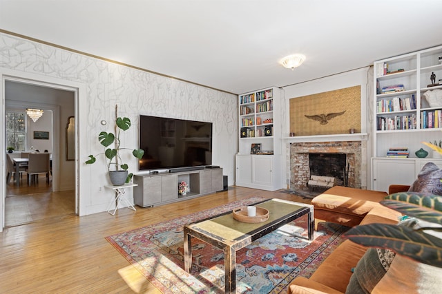 living area featuring built in features, wood finished floors, wallpapered walls, ornamental molding, and a brick fireplace