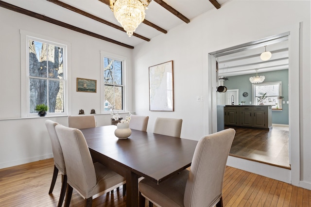 dining area with beam ceiling, light wood-style flooring, plenty of natural light, and a chandelier