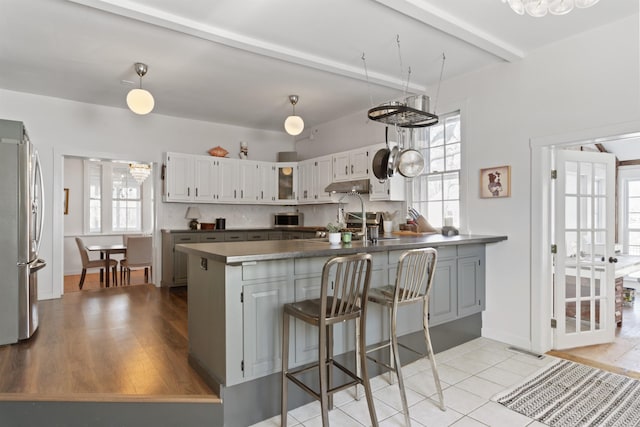 kitchen with under cabinet range hood, stainless steel appliances, backsplash, and dark countertops