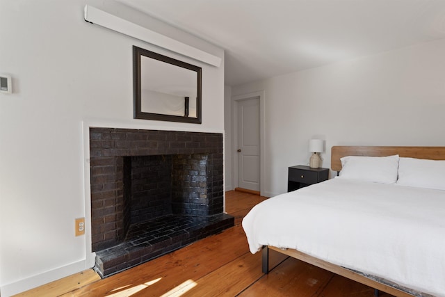 bedroom with wood finished floors, a fireplace, and baseboards