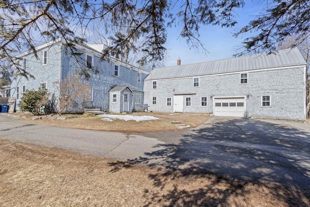 back of property featuring aphalt driveway, a chimney, and metal roof