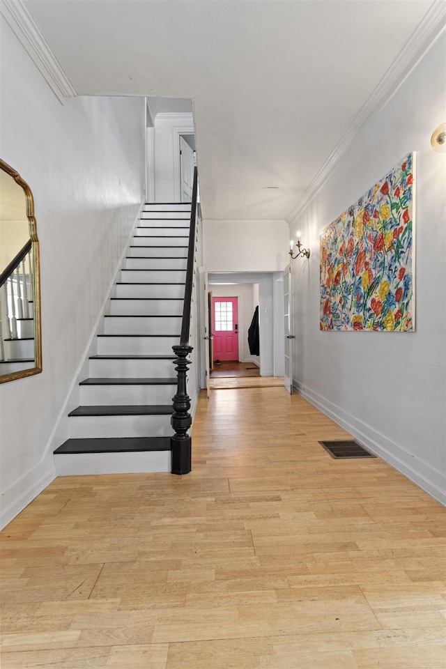 stairs with crown molding, wood finished floors, visible vents, and baseboards