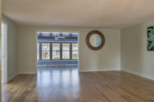 empty room with ceiling fan, a baseboard heating unit, baseboards, and wood finished floors