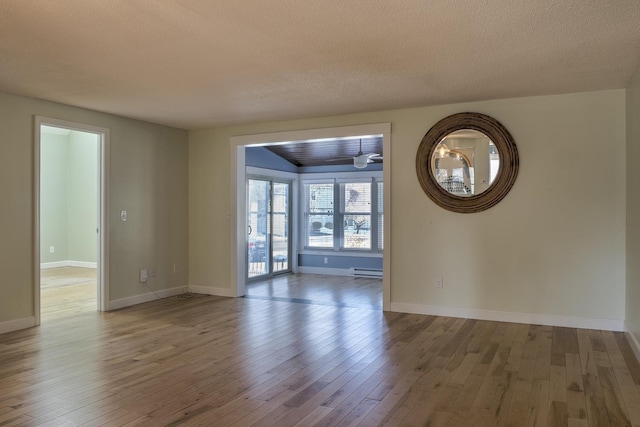 empty room featuring a baseboard heating unit, baseboards, a textured ceiling, and hardwood / wood-style flooring