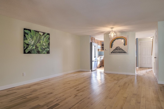 spare room with baseboards, light wood finished floors, and a textured ceiling