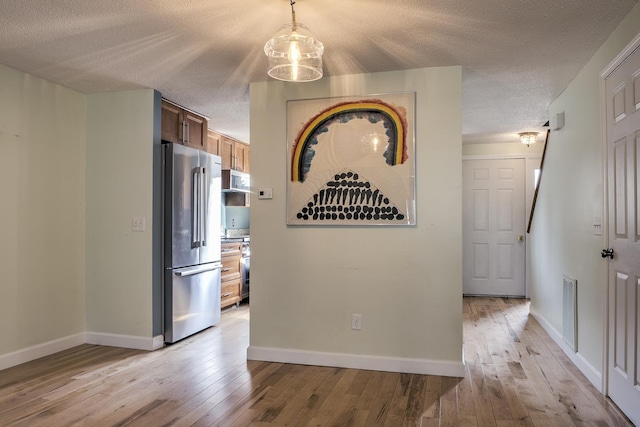 hallway with visible vents, baseboards, light wood-style floors, and a textured ceiling