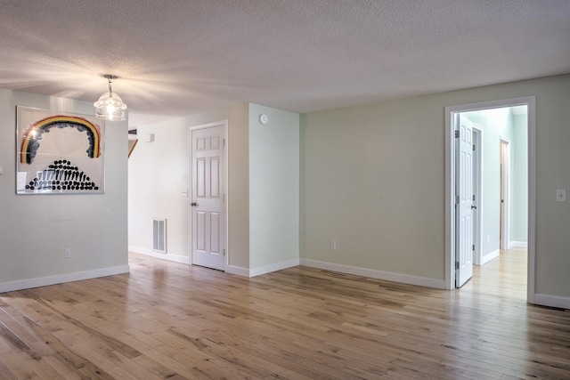 spare room with visible vents, a textured ceiling, baseboards, and hardwood / wood-style flooring