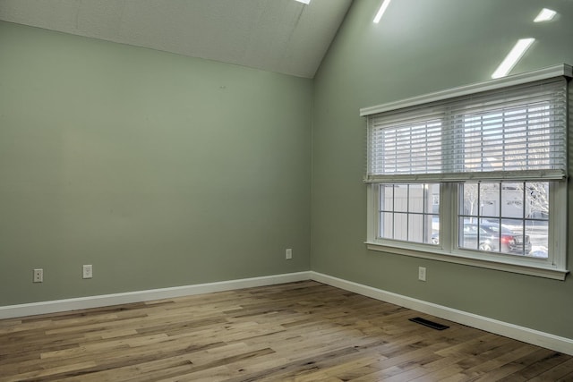 empty room with visible vents, baseboards, wood finished floors, and vaulted ceiling