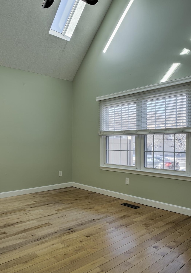 spare room featuring visible vents, lofted ceiling with skylight, a healthy amount of sunlight, and hardwood / wood-style flooring