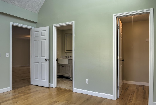 unfurnished bedroom featuring baseboards, light wood-style flooring, a sink, a closet, and a walk in closet