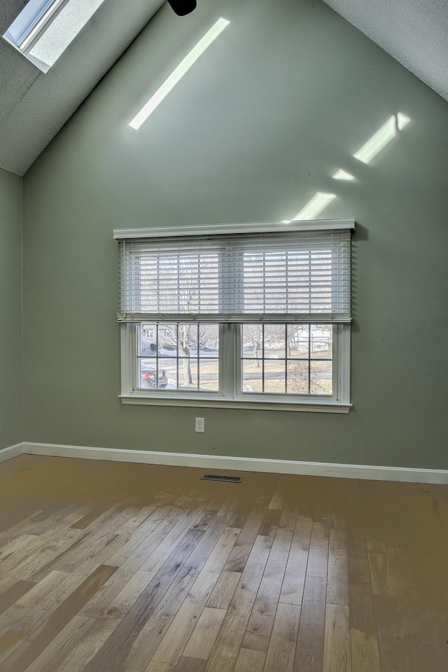 spare room with lofted ceiling with skylight, baseboards, visible vents, and wood-type flooring