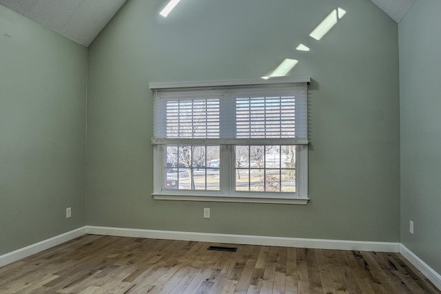 unfurnished room with visible vents, wood finished floors, baseboards, and vaulted ceiling