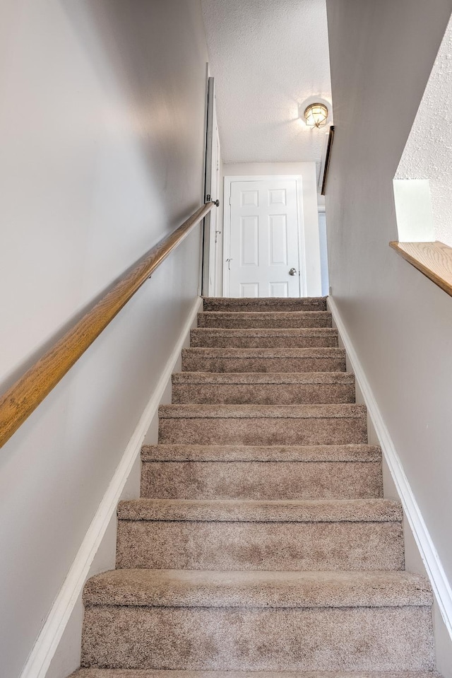 stairway with baseboards and a textured ceiling