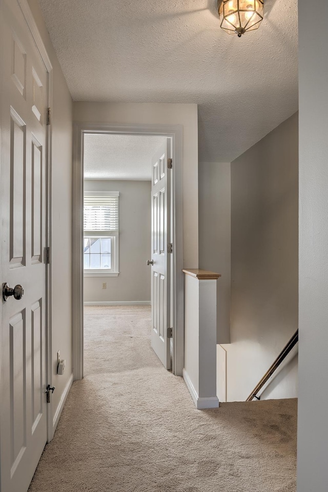 corridor with carpet flooring, an upstairs landing, baseboards, and a textured ceiling