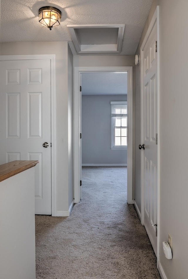 corridor featuring baseboards, carpet, attic access, and a textured ceiling