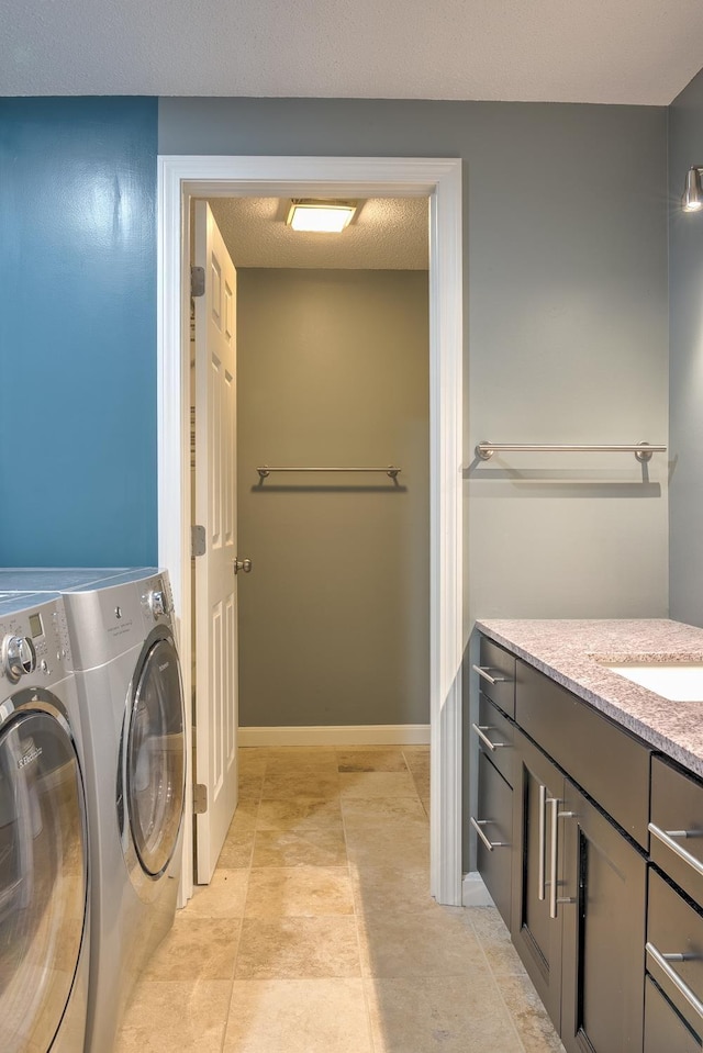 washroom featuring baseboards, laundry area, separate washer and dryer, a sink, and a textured ceiling