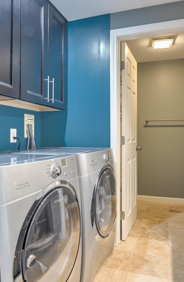 clothes washing area featuring baseboards, cabinet space, a textured ceiling, and washing machine and clothes dryer