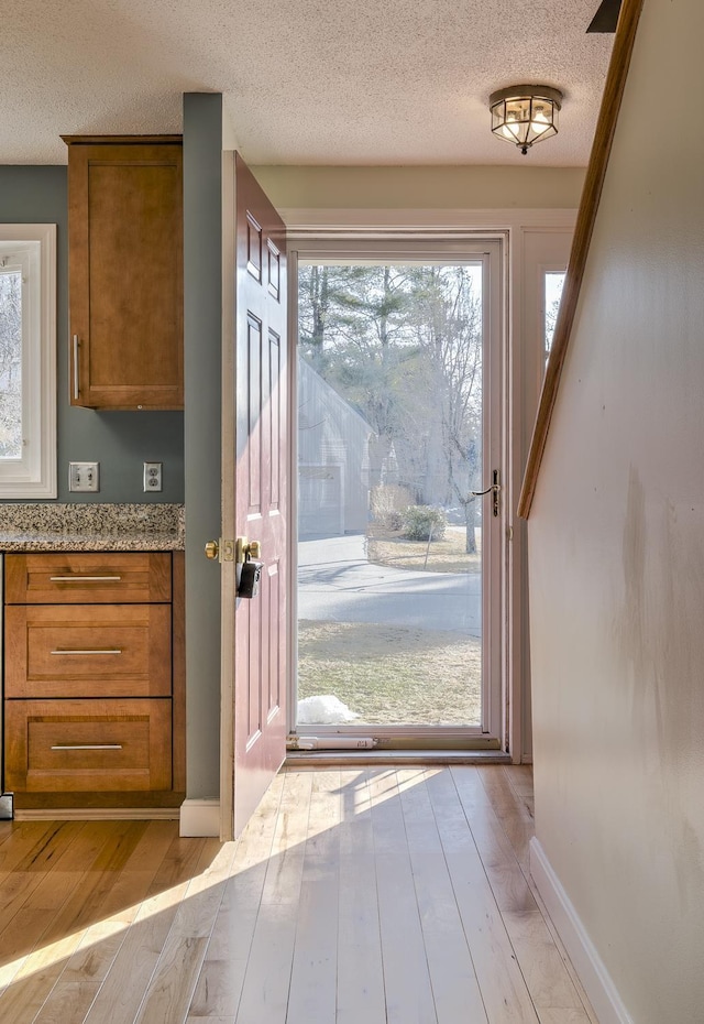 doorway featuring baseboards, light wood-type flooring, and a textured ceiling