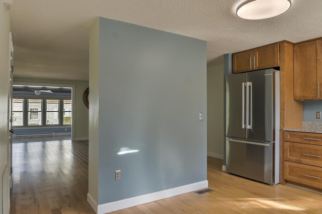 kitchen with baseboards, high end refrigerator, light wood-style flooring, brown cabinetry, and a textured ceiling