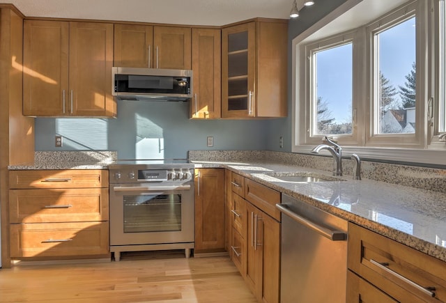 kitchen with brown cabinets, light wood-style flooring, light stone counters, a sink, and stainless steel appliances