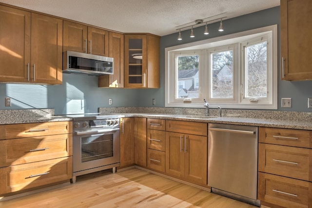 kitchen with brown cabinets, a textured ceiling, stainless steel appliances, light wood-style floors, and glass insert cabinets