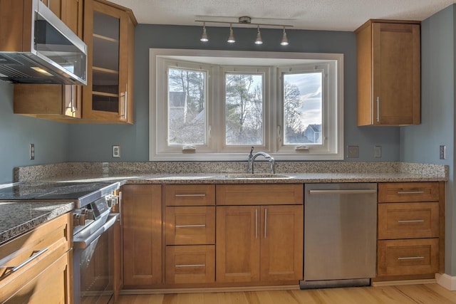 kitchen with brown cabinets, light wood-style flooring, a sink, appliances with stainless steel finishes, and stone counters