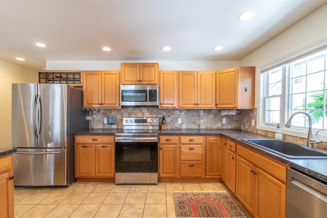 kitchen with light tile patterned flooring, a sink, decorative backsplash, appliances with stainless steel finishes, and dark countertops