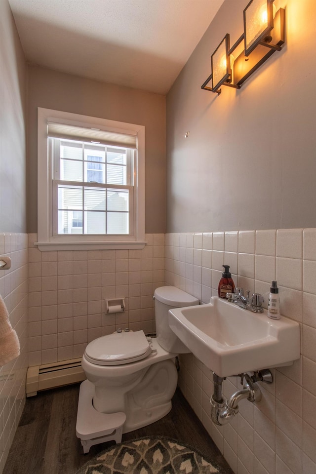 half bath featuring wood finished floors, wainscoting, a baseboard heating unit, tile walls, and toilet