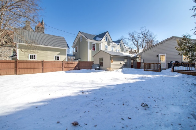 snow covered property featuring metal roof, a garage, a wooden deck, and fence