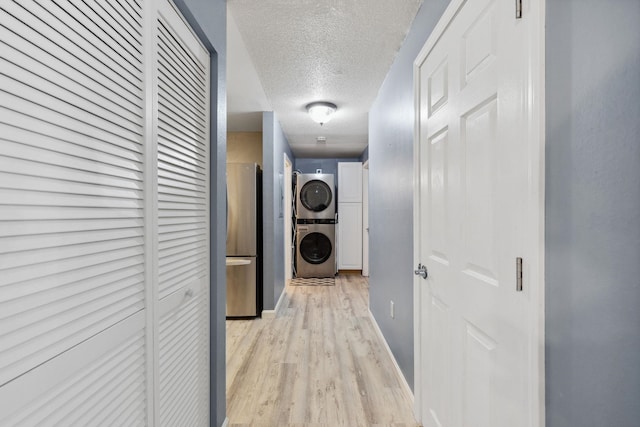 hall with light wood-style flooring, a textured ceiling, and stacked washer / drying machine