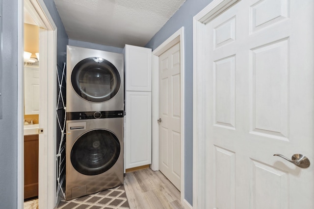 washroom with cabinet space, a textured ceiling, stacked washer / drying machine, and light wood-style floors