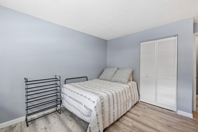 bedroom with a closet, a textured ceiling, baseboards, and wood finished floors