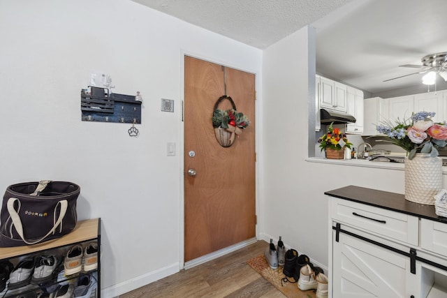 doorway to outside with ceiling fan, wood finished floors, baseboards, and a textured ceiling