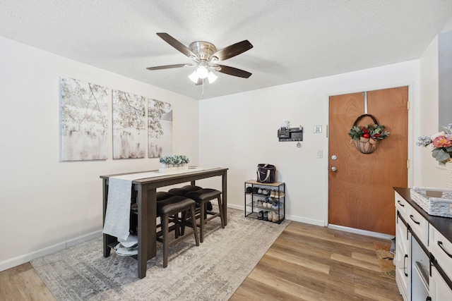 dining space featuring a textured ceiling, light wood-type flooring, baseboards, and a ceiling fan