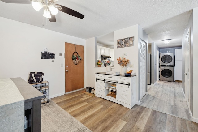 interior space with stacked washer / dryer, baseboards, light wood-style floors, a textured ceiling, and white cabinetry