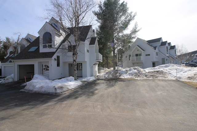 view of snow covered exterior featuring a balcony, an attached garage, and a residential view