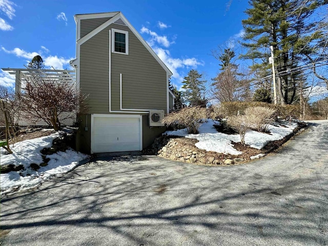 view of snowy exterior featuring an attached garage and ac unit