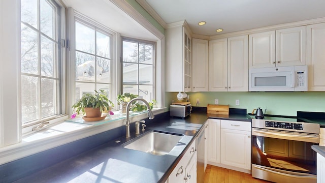 kitchen featuring dark countertops, glass insert cabinets, stainless steel appliances, white cabinetry, and a sink