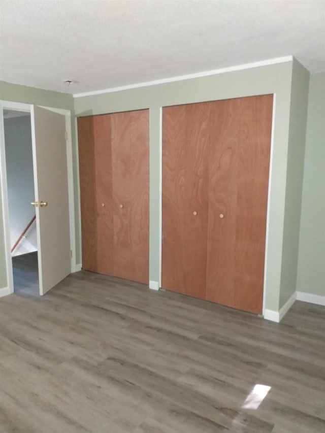 unfurnished bedroom with wood finished floors, baseboards, and two closets