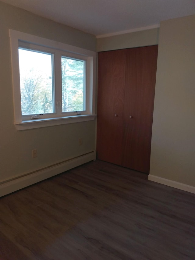 unfurnished bedroom with a closet, baseboards, baseboard heating, and wood finished floors