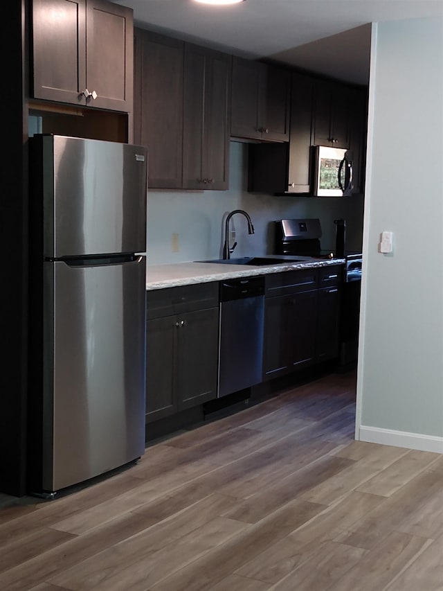 kitchen with a sink, freestanding refrigerator, light wood-style floors, light countertops, and dishwashing machine