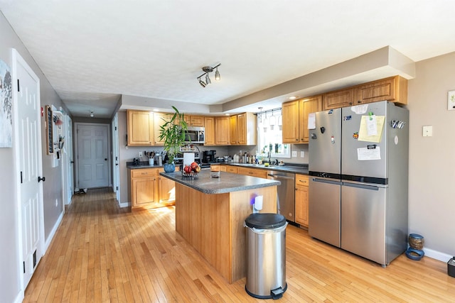 kitchen with baseboards, a kitchen island, light wood-style flooring, appliances with stainless steel finishes, and dark countertops