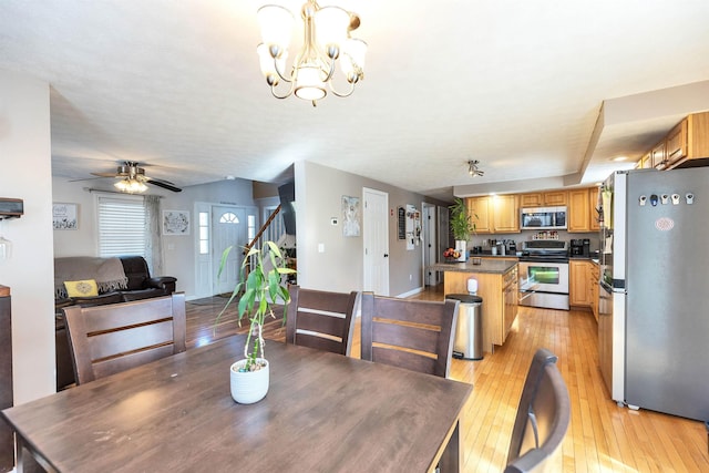 dining area featuring stairway, ceiling fan with notable chandelier, and light wood finished floors