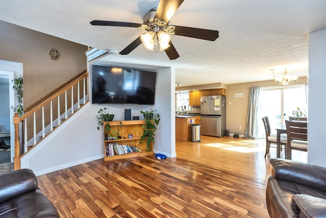 living area with stairs, light wood-style flooring, ceiling fan with notable chandelier, and baseboards