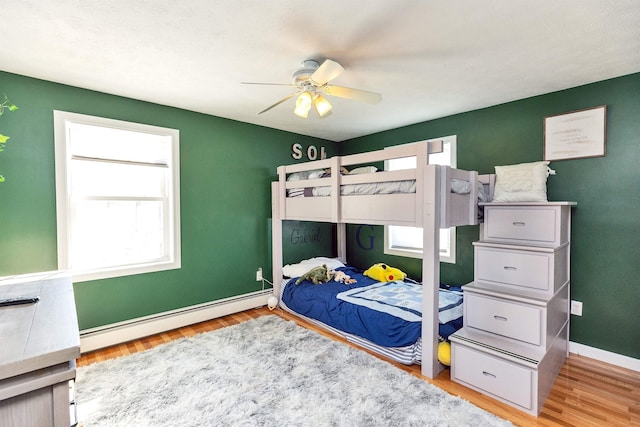 bedroom with a ceiling fan, wood finished floors, baseboards, and baseboard heating