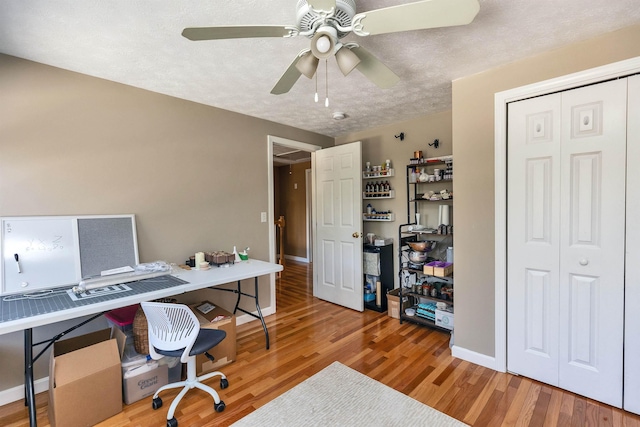 home office featuring a textured ceiling, a ceiling fan, baseboards, and wood finished floors