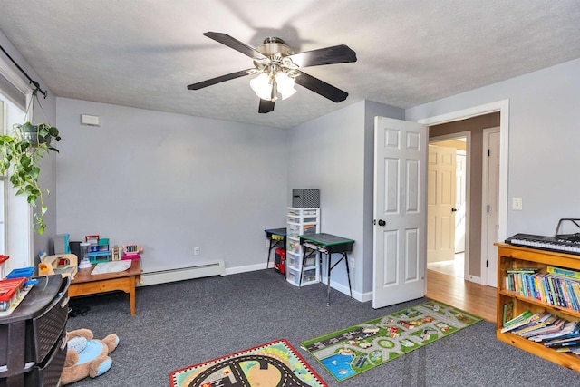 playroom featuring a textured ceiling, carpet flooring, a baseboard radiator, baseboards, and ceiling fan