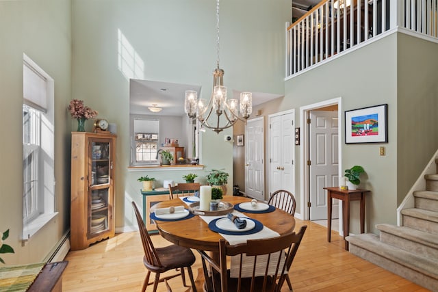 dining space with stairs, an inviting chandelier, light wood-style floors, and a towering ceiling