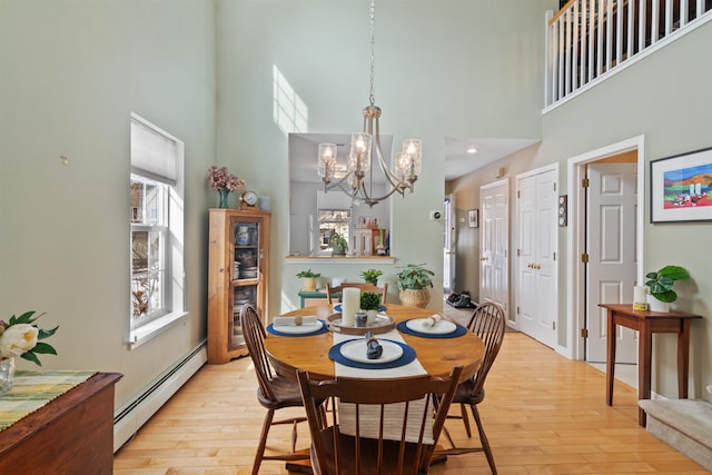 dining room featuring light wood-type flooring, a baseboard radiator, and a towering ceiling